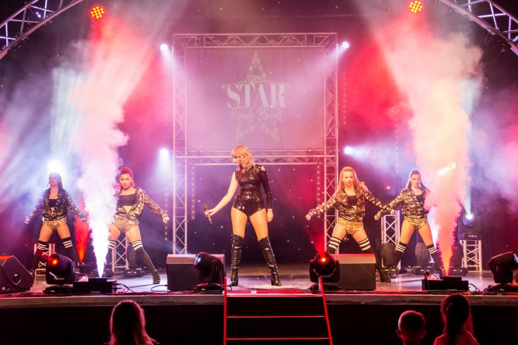 A tribute act dressed as Taylor Swift is surrounded by dancers.